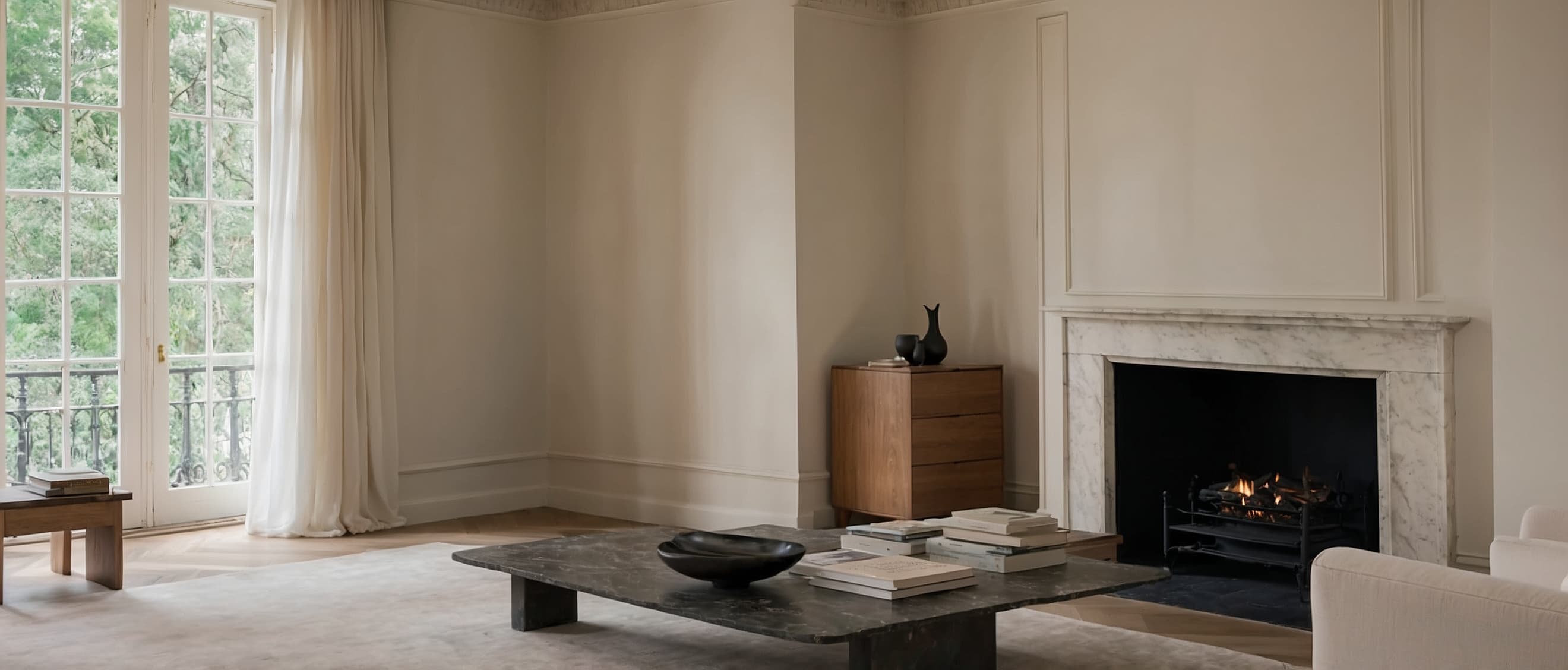 Tall-ceilinged room with boiserie walls, limestone fireplace, and two lit floor lamps at dusk